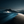 Blue-grey desert sand dunes with rippled textures, pale light and distant mountains beneath a dark sky.