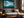 Blue mountain lake artwork in a slim wood frame above a gray sofa beside a window.