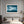 Light wood-framed mountain lake print above a bed beside a lit fireplace.
