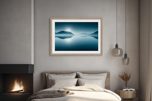 Light wood-framed mountain lake print above a bed beside a lit fireplace.