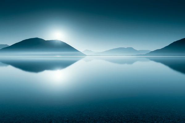 Minimalist blue landscape of mountain silhouettes reflected in a calm lake beneath a bright horizon.