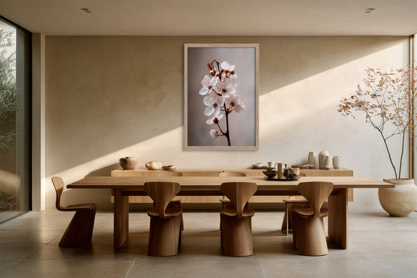 Light wood-framed cherry blossom print above a long wooden dining table and sculptural chairs.