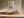 Light wood-framed cherry blossom print above a low wooden sideboard in angled sunlight.