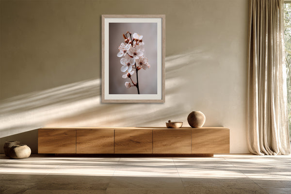 Light wood-framed cherry blossom print above a low wooden sideboard in angled sunlight.