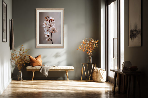 Light wood-framed cherry blossom print above a bench with an orange cushion by tall windows.