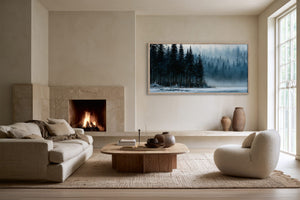 Framed misty evergreen lake artwork displayed beside a lit fireplace and low seating area.