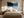 Framed evergreen forest and frozen lake artwork above a white bed between two bedside lamps.