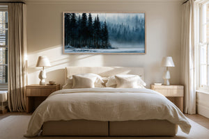 Framed evergreen forest and frozen lake artwork above a white bed between two bedside lamps.