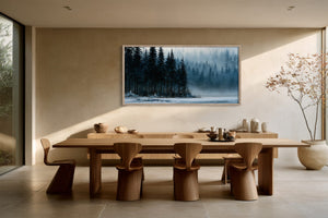 Framed misty forest lake artwork above a long wooden dining table and sculptural chairs.