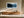 White-framed winter forest artwork above a low wooden credenza in a sunlit interior.