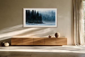 White-framed winter forest artwork above a low wooden credenza in a sunlit interior.