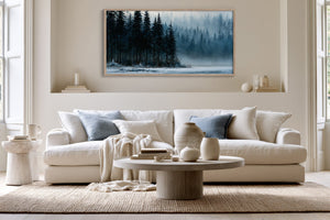Framed misty evergreen lake artwork above a white sofa with pale blue cushions.