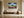 Framed mountain ridge artwork above a wooden bench and large ceramic vessel near a window.