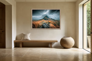 Framed mountain ridge artwork above a wooden bench and large ceramic vessel near a window.