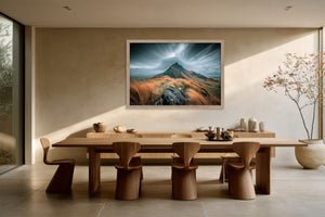 Framed mountain ridge artwork above a long wooden dining table with sculptural chairs.
