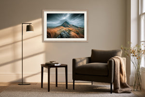 Framed mountain ridge artwork above a dark armchair, side table, and floor lamp.