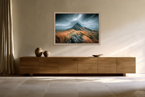 Framed mountain ridge artwork hung above a long wooden sideboard with ceramic vases.