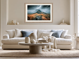 Framed stormy mountain ridge artwork displayed above a white sofa with blue cushions.