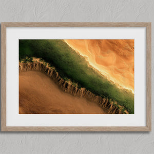 Aerial view of dense green vegetation meeting sculpted golden desert sand.
