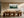 Framed misty pine forest watercolor displayed above a long wooden dining table with sculptural chairs.