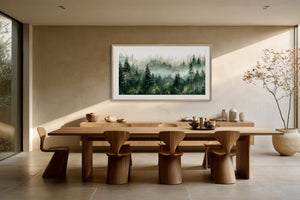 Framed misty pine forest watercolor displayed above a long wooden dining table with sculptural chairs.
