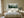 Framed misty pine forest watercolor above a neatly made bed between two wooden nightstands.