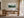 Framed misty pine forest watercolor above a wooden desk with a chair and black task lamp.