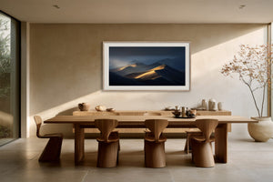 White-framed dune artwork displayed above a long wooden dining table with sculptural chairs.