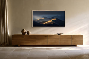 Framed dune artwork above a low wooden sideboard with two ceramic vessels.