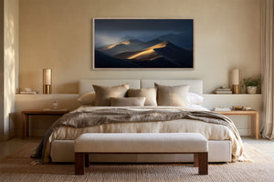 Framed dune artwork centered above a bed with neutral bedding and a bench.