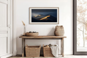 White-framed dune artwork above a rustic console table with woven baskets.
