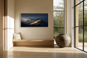 Framed dune artwork above a built-in bench beside floor-to-ceiling black-framed windows.