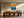 Framed golden sun and teal wave illustration above a long wooden dining table.
