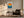 Framed sun and ocean illustration beside a dark armchair and floor lamp.