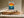 Framed golden sun over teal waves illustration above a low wooden sideboard.