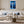White-framed blue forest print above a white sofa and round wooden coffee table.
