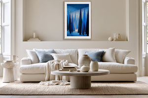 White-framed blue forest print above a white sofa and round wooden coffee table.