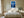 White-framed blue conifer artwork above a bed with white linens and wooden nightstands.