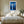 White-framed blue conifer artwork above a bed with white linens and wooden nightstands.