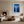 White-framed forest print displayed between a fireplace and tall window in a living room.
