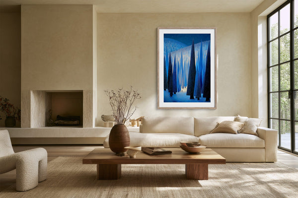 White-framed blue forest artwork above a cream sofa beside large grid windows.