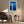 White-framed blue conifer artwork above an upholstered armchair, side table, and floor lamp.