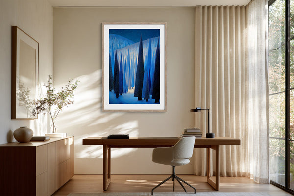 White-framed blue forest print above a wooden desk and swivel chair by sheer curtains.