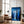 Large black-framed blue forest artwork leaning beside a brown armchair and floor lamp.