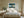 Leaning Light tree artwork in a pale wood frame above a bed with white linens.
