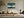 Leaning Light tree artwork in a pale wood frame above a white sofa and low coffee table.