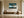 Leaning Light tree artwork in a pale wood frame above a wooden bench beside a large ceramic vessel.