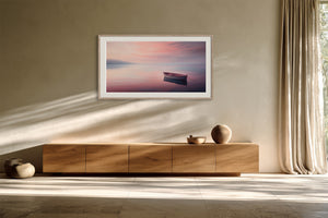 White-framed boat artwork above a wooden sideboard in a sunlit neutral interior.