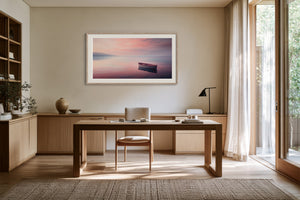 White-framed rowboat artwork displayed above a wooden desk in a bright study.