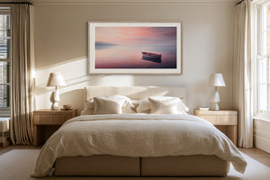 White-framed rowboat artwork centered above a bed with cream bedding and bedside tables.